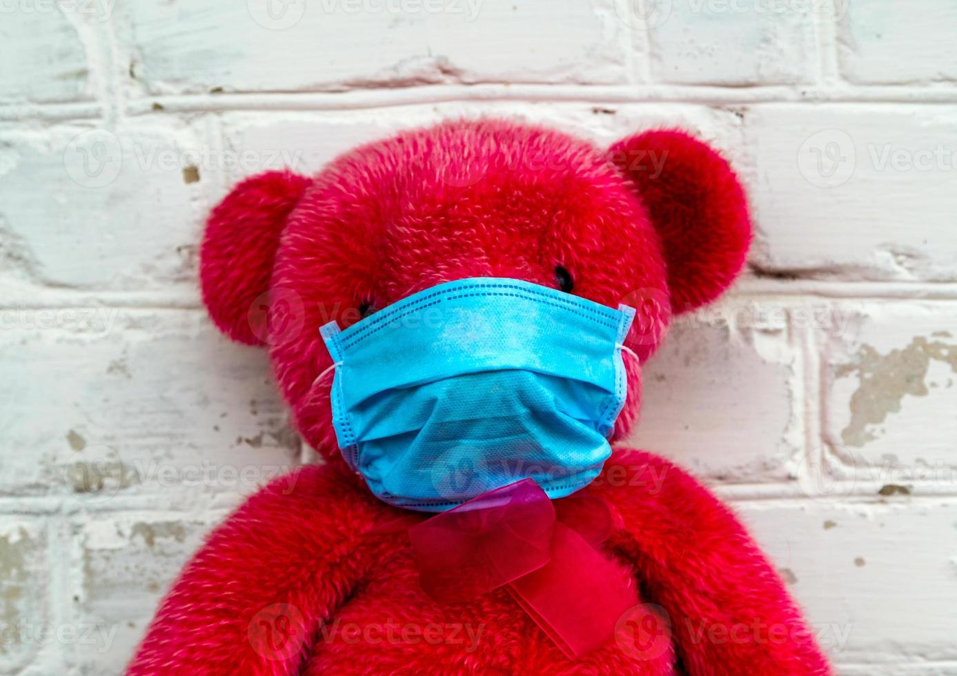 einsamer roter Teddybär in einer medizinischen Schutzmaske foto