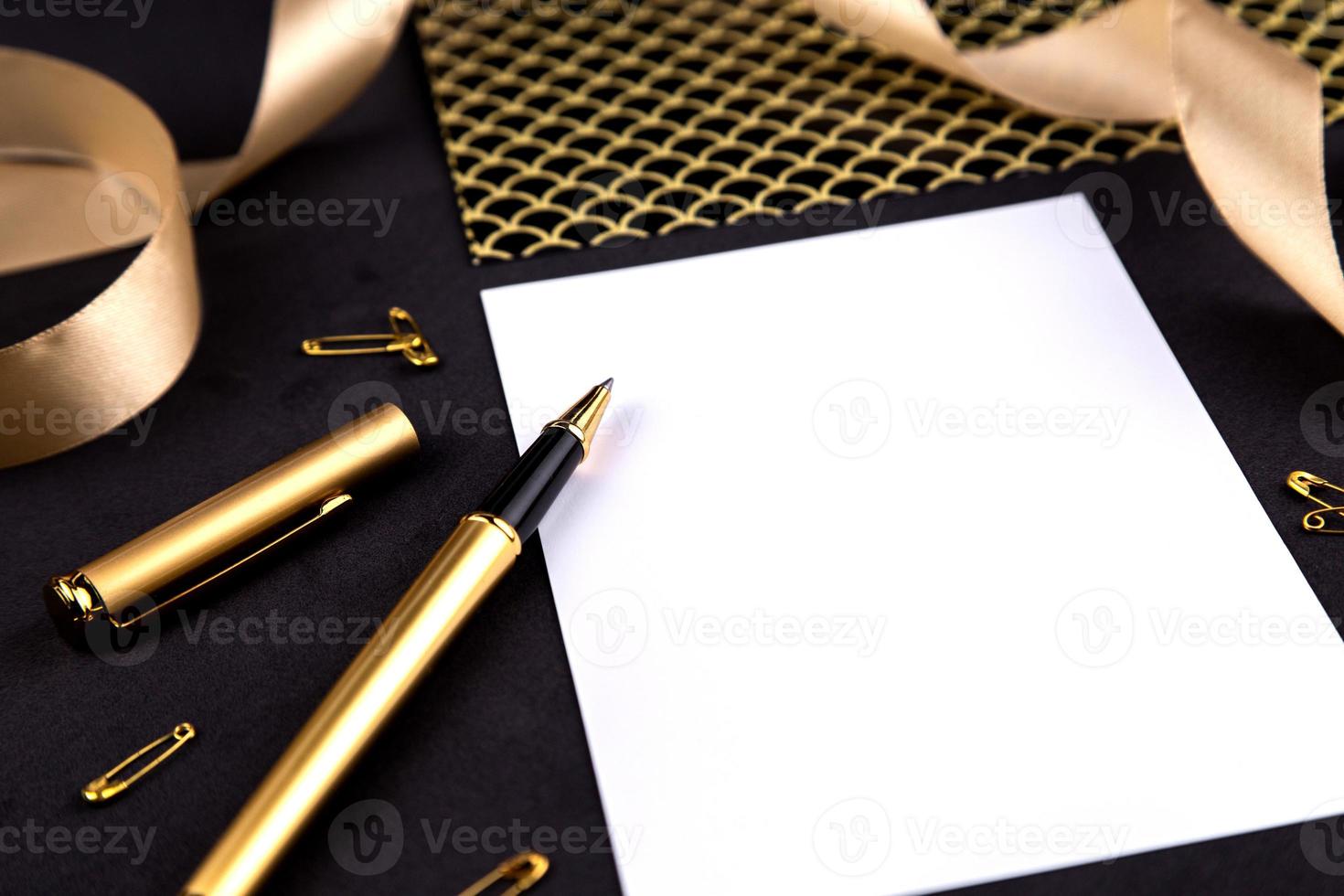 Goldstift, Band, Büroklammern und Briefpapier auf einem schwarzen Hintergrund mit einem weißen Blatt Papier mit Kopierraum foto