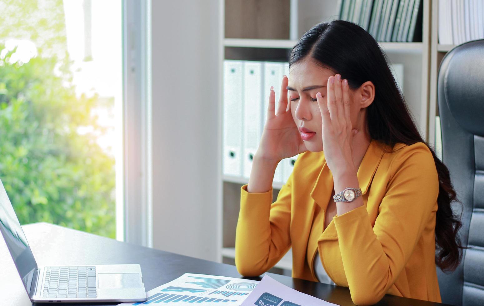 Porträt der asiatischen Frau im gelben Anzug, der im Büro sitzt und über Marketing nachdenkt foto