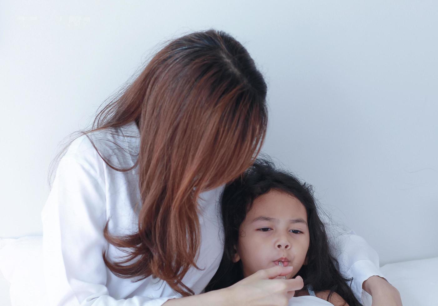asiatische Mutter misst die Temperatur ihrer Tochter foto