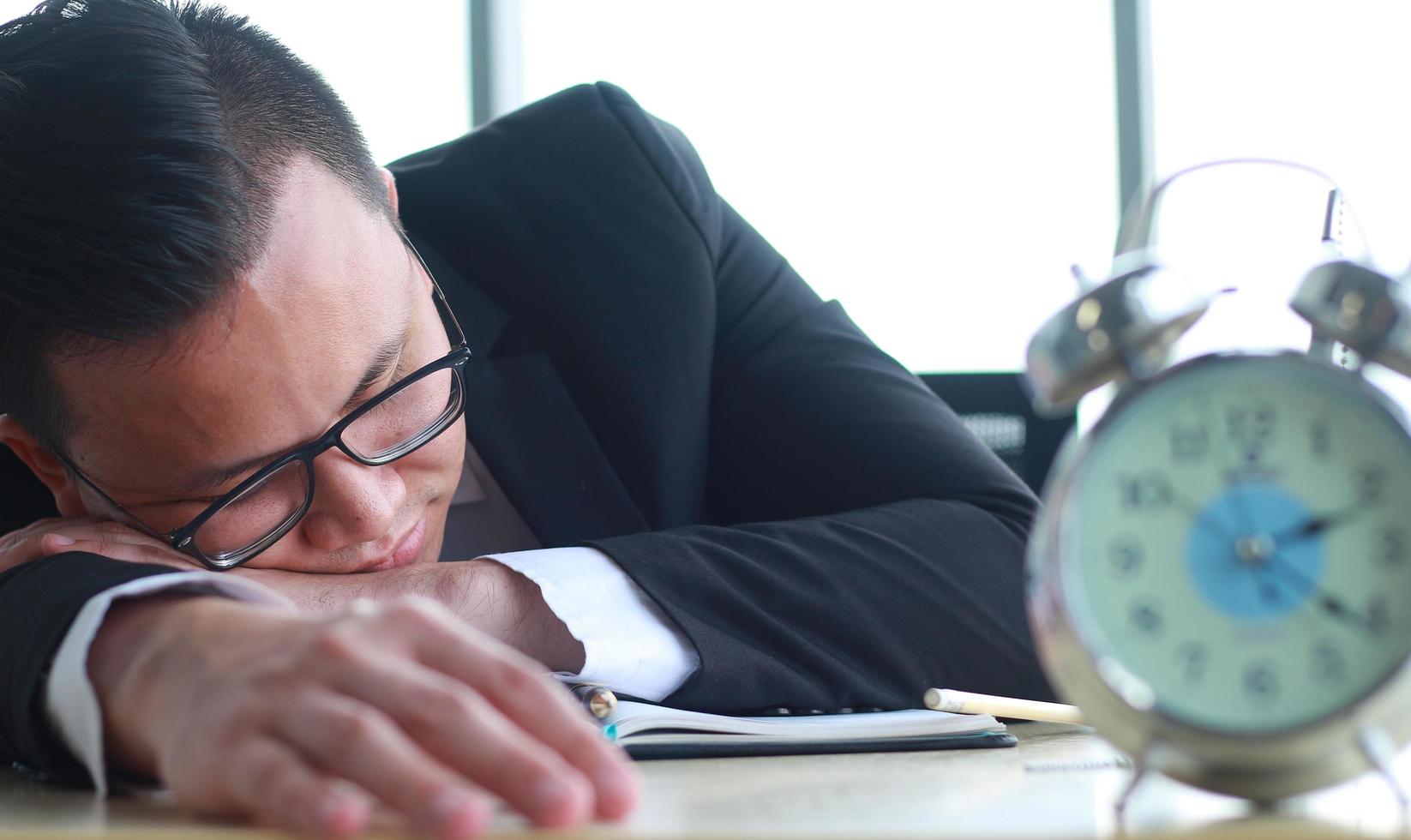 Porträt des jungen asiatischen Geschäftsmannes, der müde auf dem Schreibtisch schläft foto