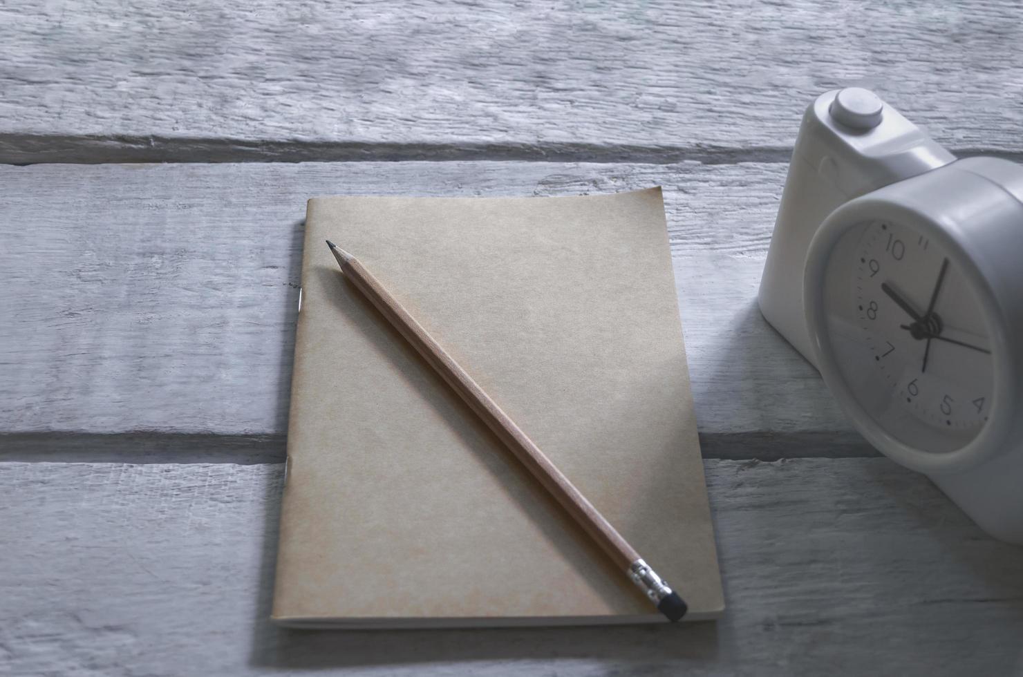 ein Buch und ein Bleistift mit Wecker auf einem alten Holztisch foto