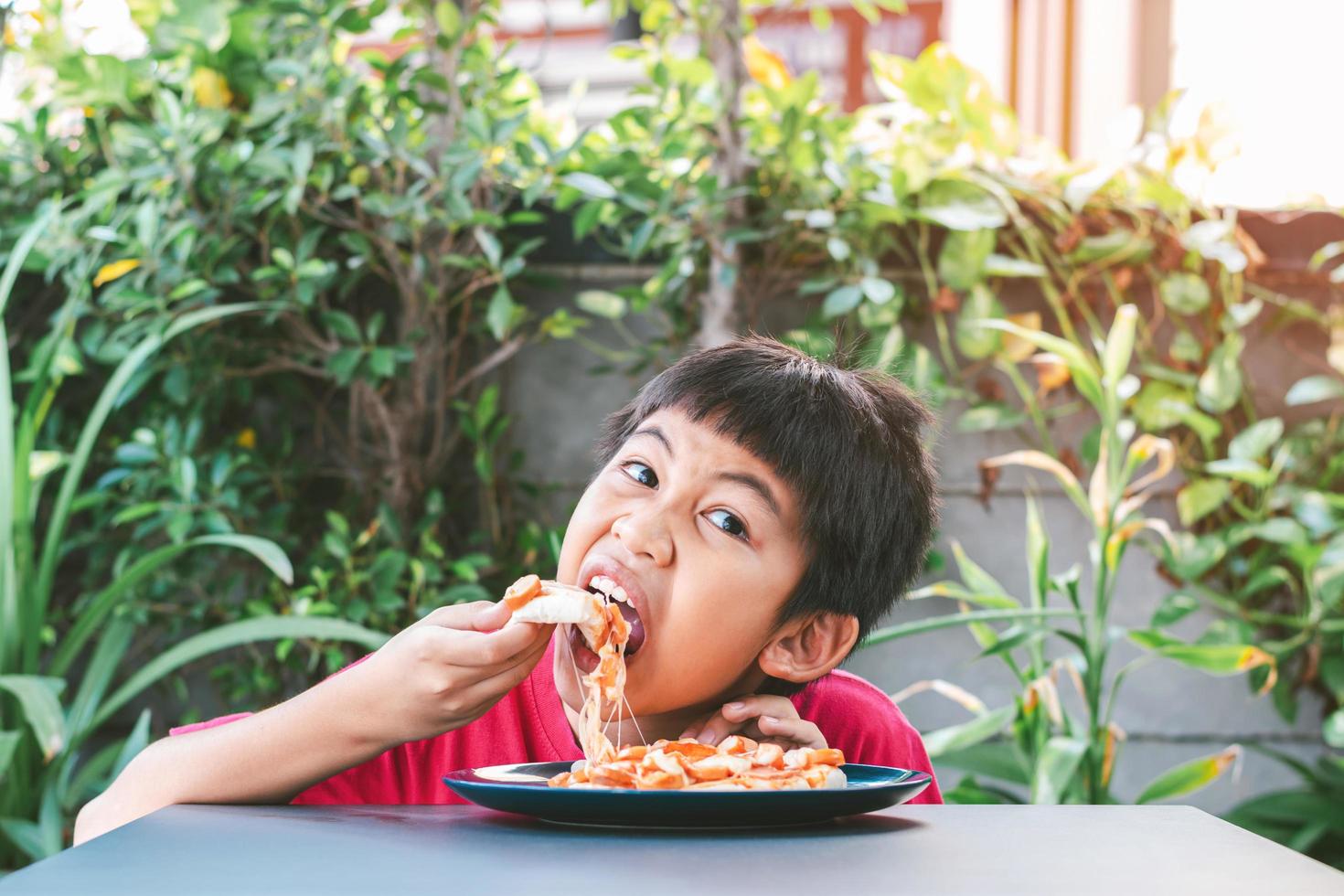 asiatischer süßer Junge, der glücklich sitzt und Pizza isst foto