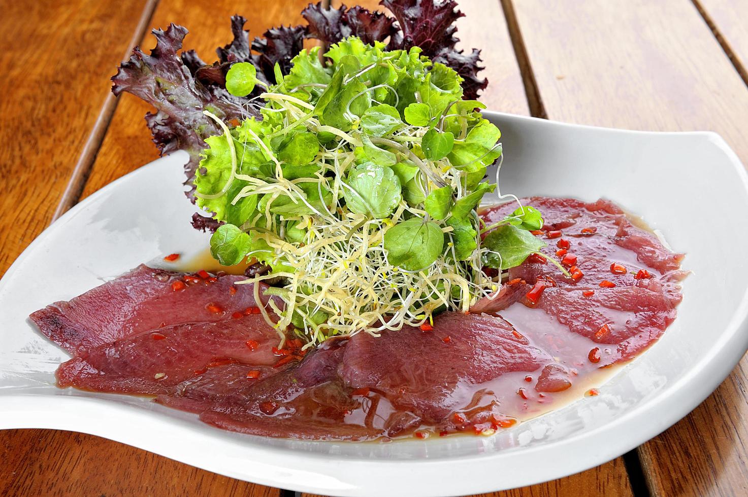 Fisch-Carpaccio mit Oliven und Salat auf einem weißen Teller foto