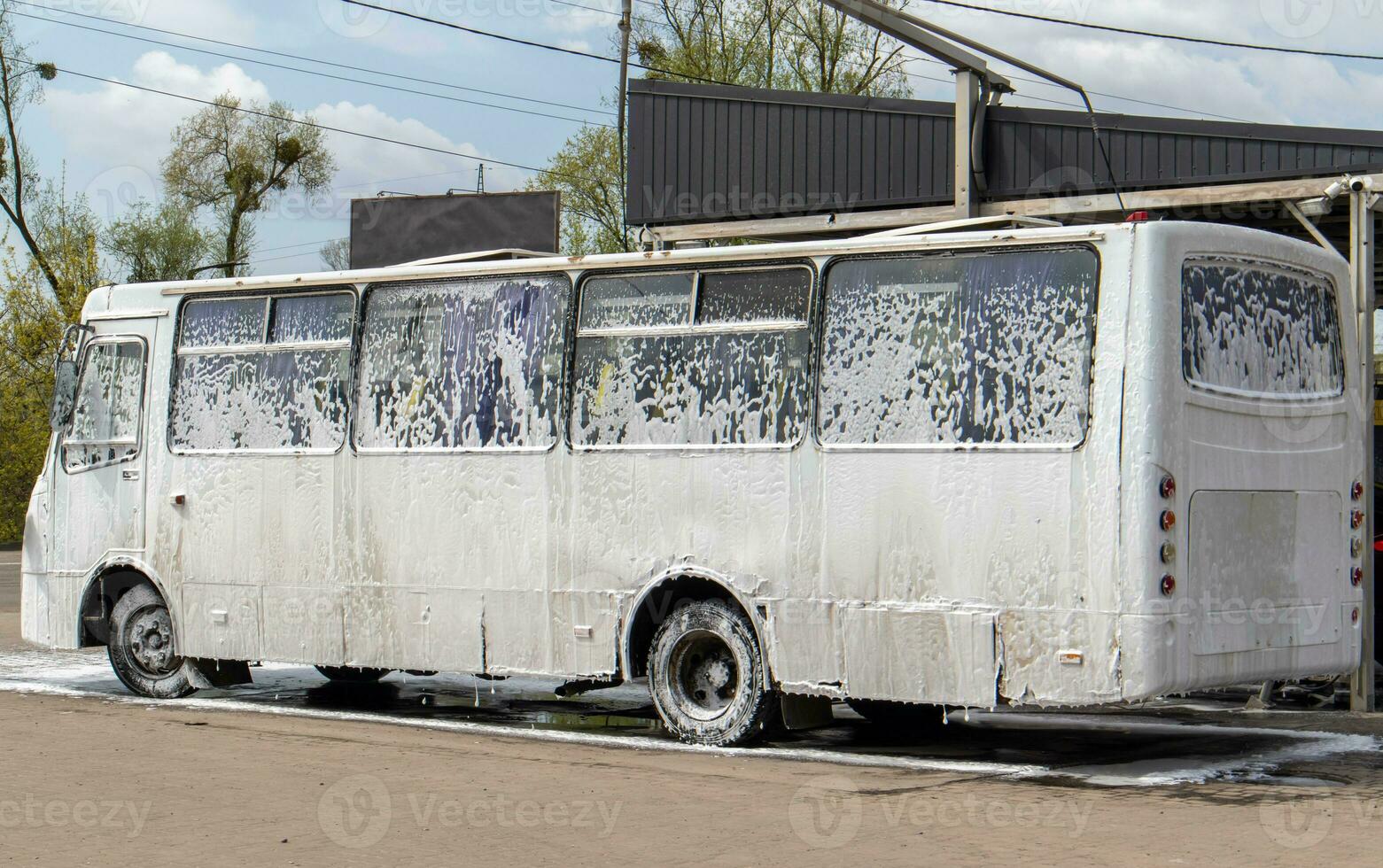 groß Weiß Bus im Schaum beim ein Selbstbedienung Auto waschen. extern Waschen von Öffentlichkeit Transport Busse. Selbstbedienung Handbuch hoher Druck Auto waschen im das öffnen Luft. foto