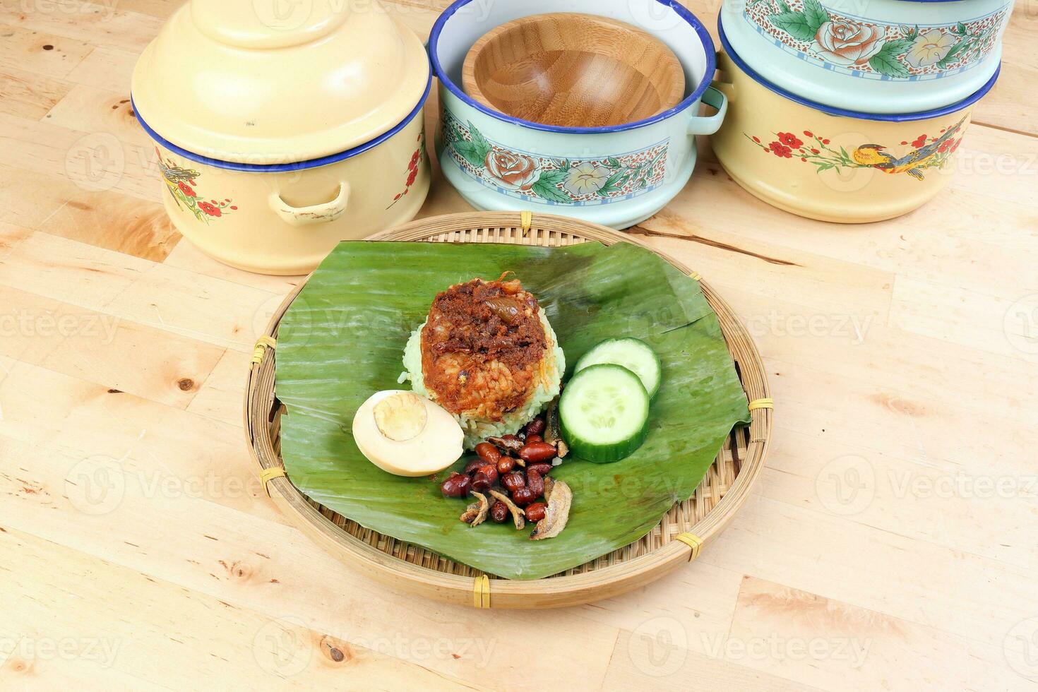 nasi Lemak duftend Reis gekocht im Kokosnuss Milch serviert mit Sambal Freund Erdnuss Anschovis gekocht Ei verpackt im Banane Blatt auf runden Bambus Teller auf hölzern Hintergrund Töpfe Behälter foto