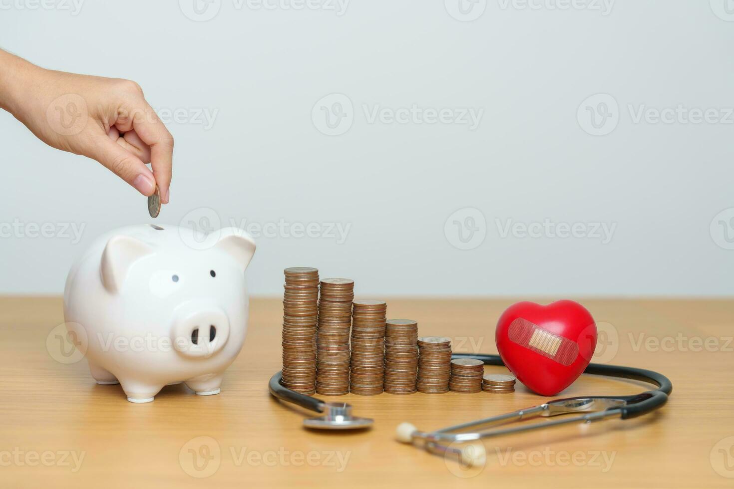 Geld sparen, Gesundheit Versicherung, medizinisch, Spende und finanziell Konzepte. Hand Putten Münze in Schweinchen Bank mit Stethoskop und Herz, Geld Stapel Zählen Anordnung zum Anzahlung und Gesundheitswesen Kosten foto