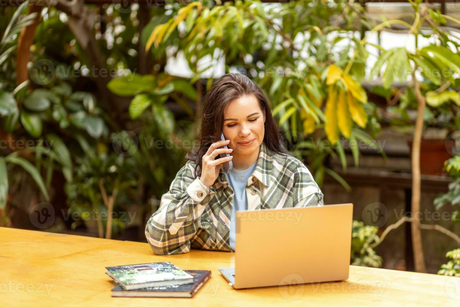 ein weiblich Florist ist reden zu Kunden auf das Telefon und Platzierung ein bestellen mit ein Laptop. Garten Center, Privat Geschäft. foto