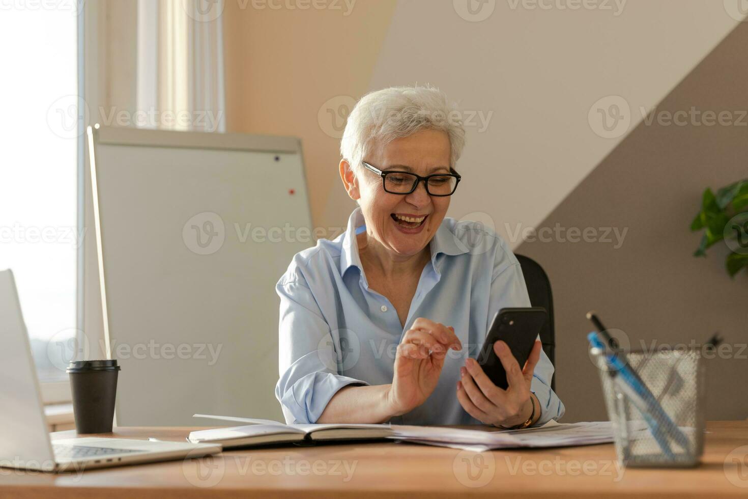 zuversichtlich stilvoll europäisch Mitte alt Senior Frau mit Smartphone beim Arbeitsplatz. stilvoll älter reifen 60er Jahre grau behaart Dame Geschäftsfrau mit Zelle Telefon im Büro. Boss Führer mit Internet Anwendungen. foto