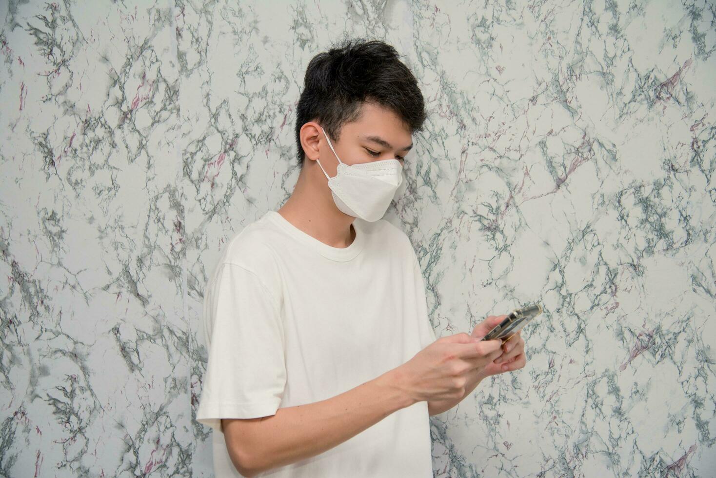 Mann setzt auf ein Gesicht Maske mit Smartphone isoliert auf Weiß Hintergrund, Pandemie und Sozial Distanzierung konzept.covid-19 foto
