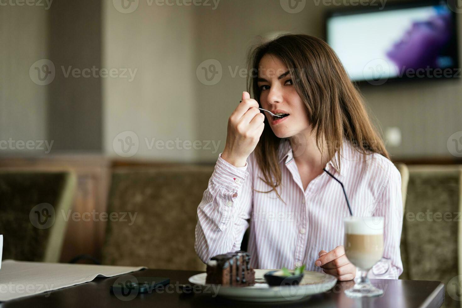 jung schön Brünette Frau sitzen im Kaffee Geschäft Cafe Restaurant drinnen und Essen Schokolade Brownie Dessert Kuchen, Gabel in der Nähe von das Mund. foto