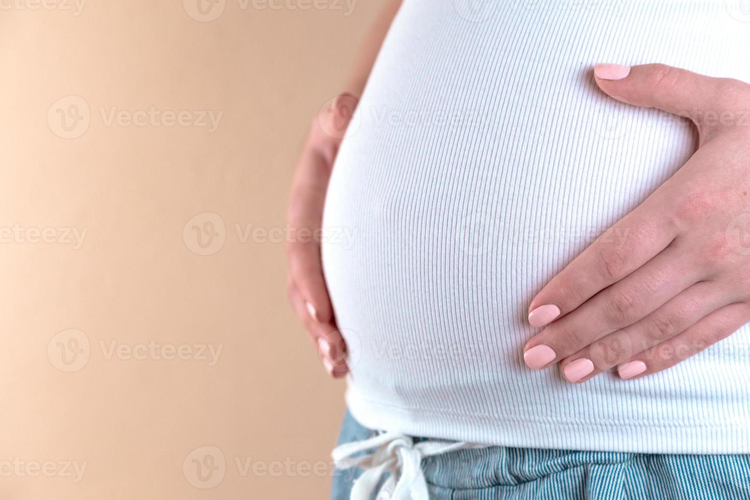 authentische Nahaufnahme einer jungen schwangeren Frau im Pyjama, die ihren Bauch streichelt foto
