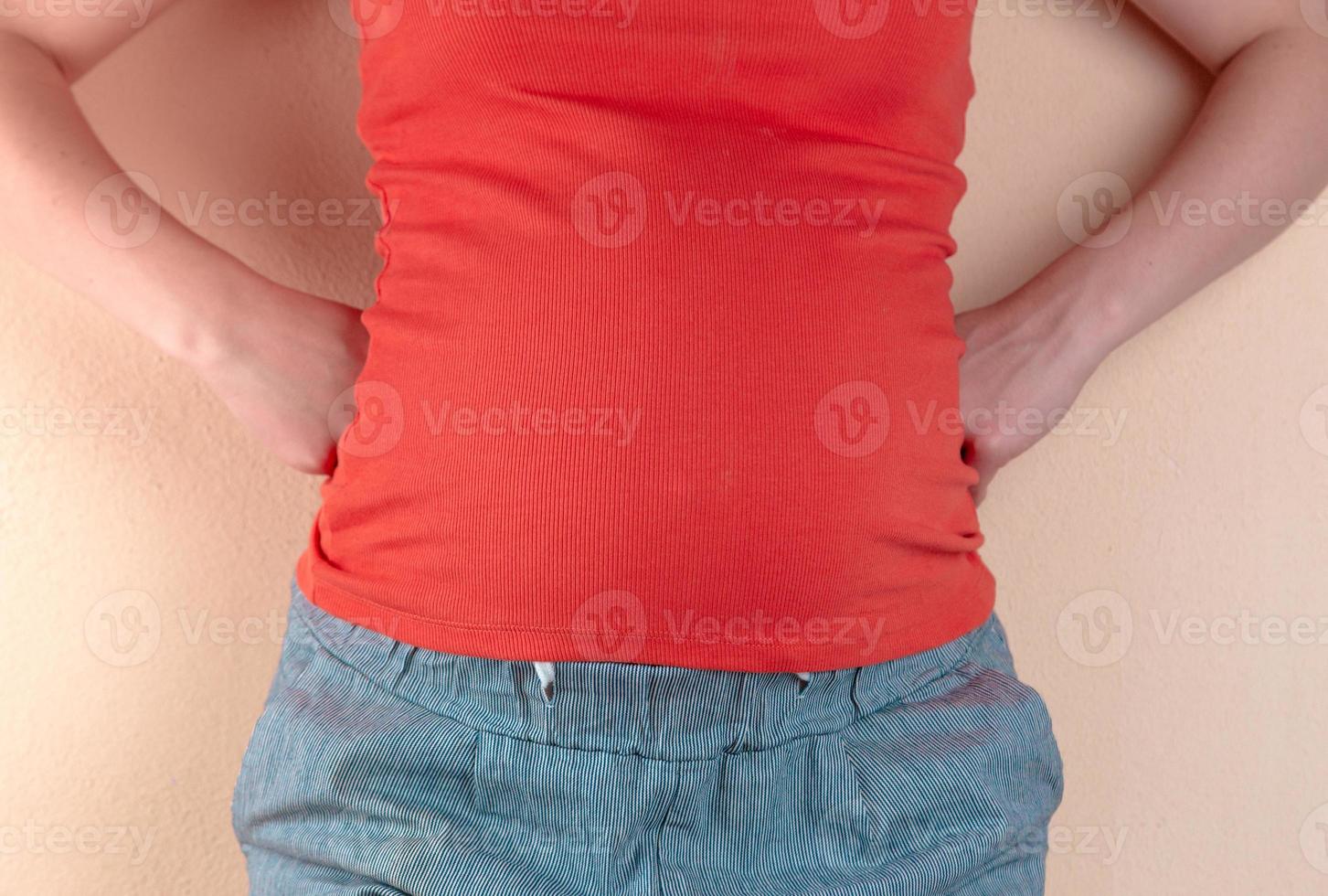 Eine junge schwangere Frau in Rot steht in der Nähe einer Wand mit den Händen hinter dem Rücken foto