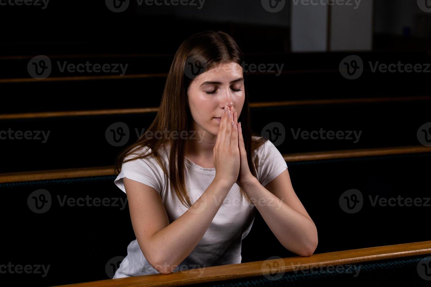 Ein christliches Mädchen im weißen Hemd betet mit demütigem Herzen in der Kirche foto