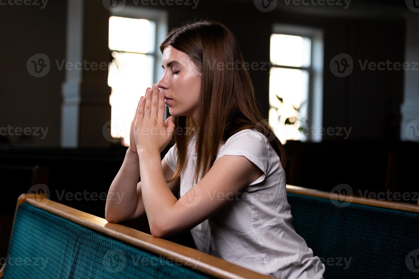 Ein christliches Mädchen im weißen Hemd sitzt und betet mit demütigem Herzen in der Kirche foto