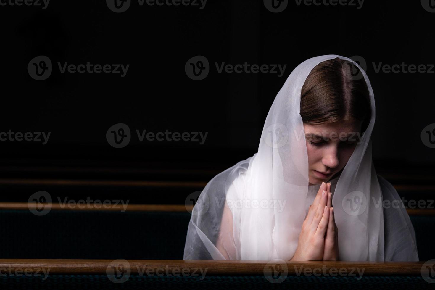 Ein junges bescheidenes Mädchen mit einem Taschentuch auf dem Kopf sitzt in der Kirche und betet foto