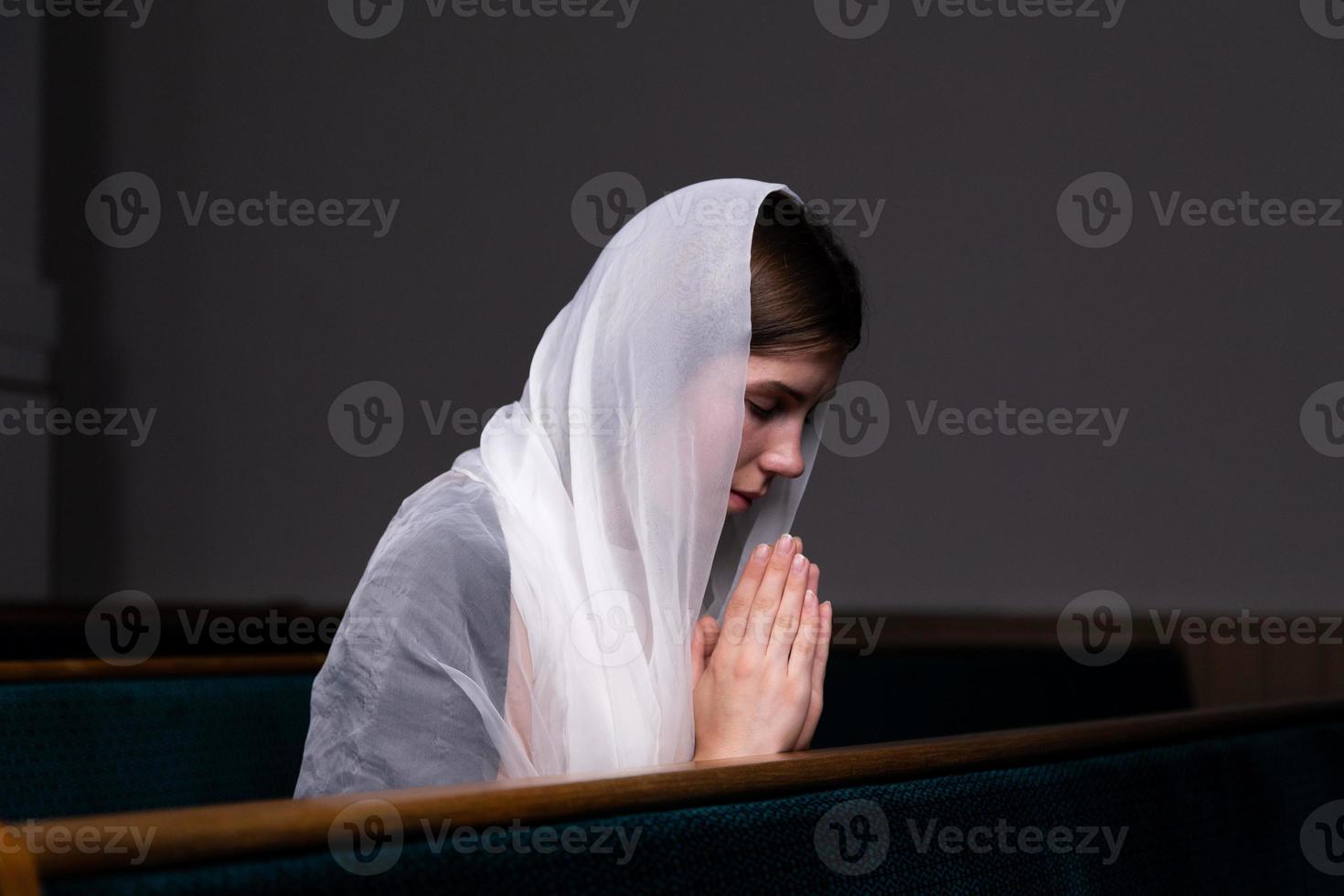 Ein junges bescheidenes Mädchen mit einem Taschentuch auf dem Kopf sitzt in der Kirche und betet foto