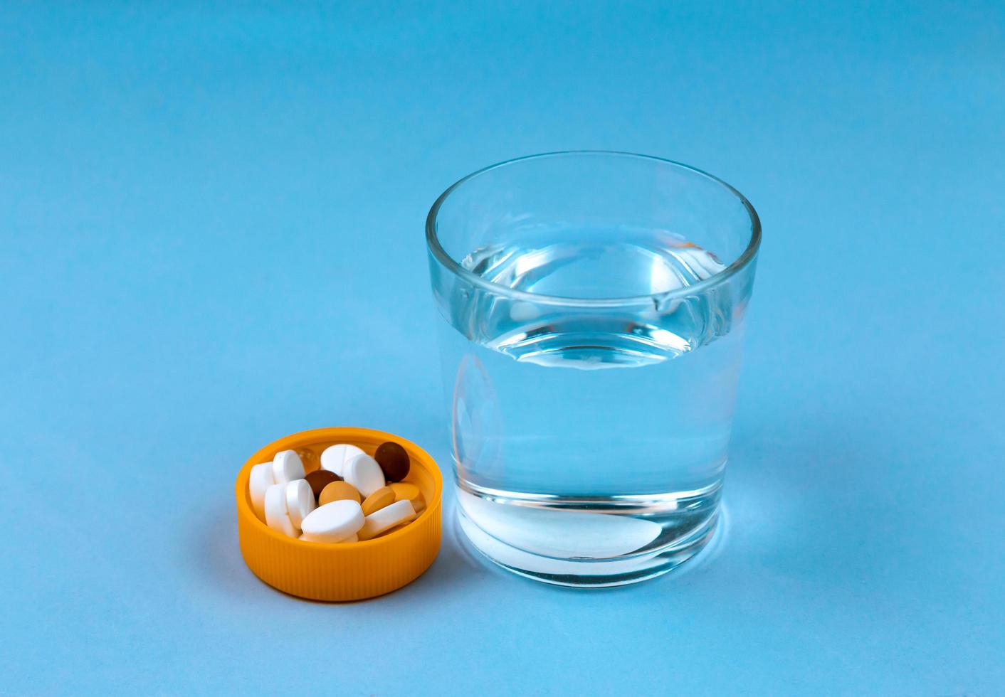 Glas Wasser und Pillen auf blauem Hintergrund mit Kopierraum für Text foto