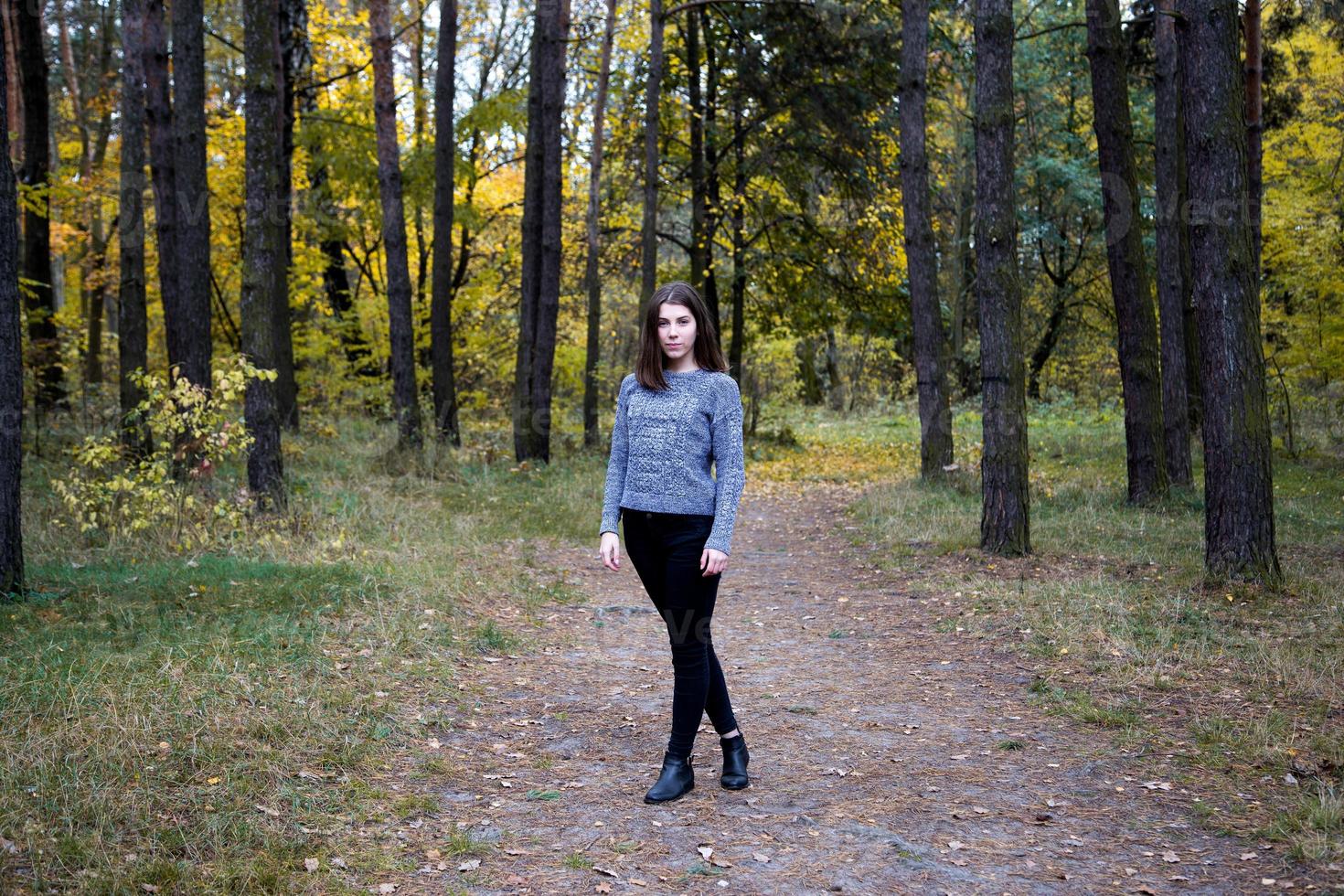 süßes Mädchen in einem grauen Pullover mit Zahnspangen auf den Zähnen, die auf der Straße im Herbstwald stehen foto