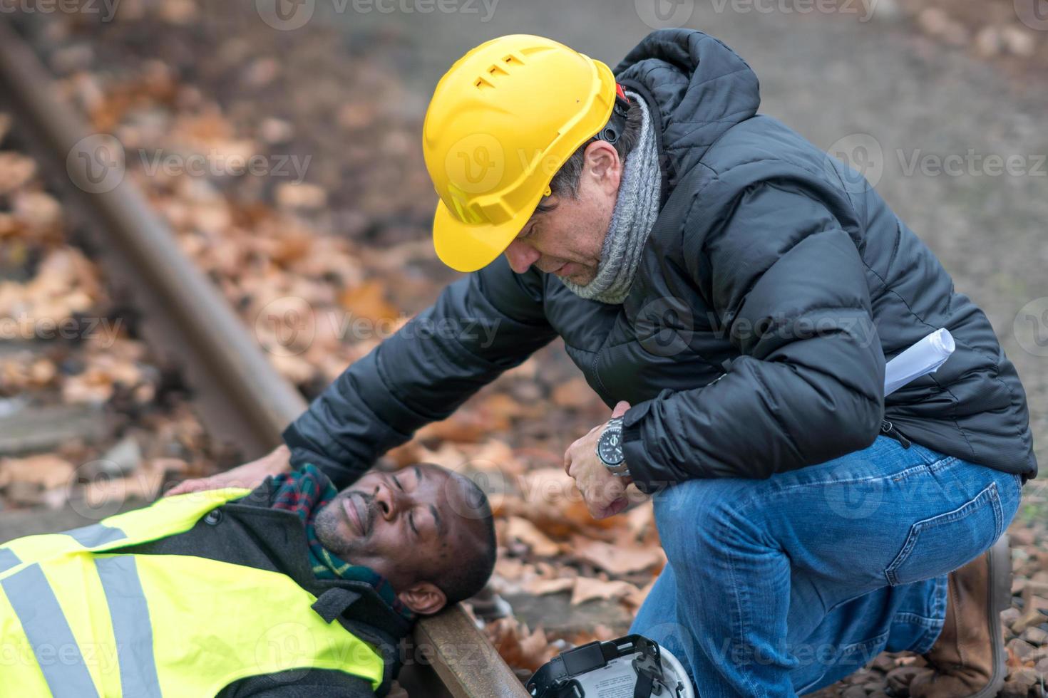 afroamerikanischer eisenbahningenieur verletzt bei einem unfall bei der arbeit auf den schienengleisen sein mitarbeiter hilft ihm foto