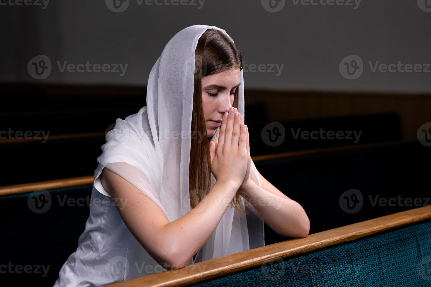 Ein junges bescheidenes Mädchen mit einem Taschentuch auf dem Kopf sitzt in der Kirche und betet foto