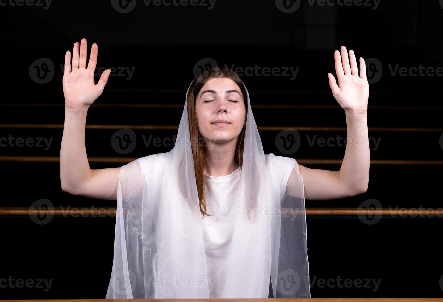 Ein junges bescheidenes Mädchen mit einem Taschentuch auf dem Kopf sitzt in der Kirche und betet foto