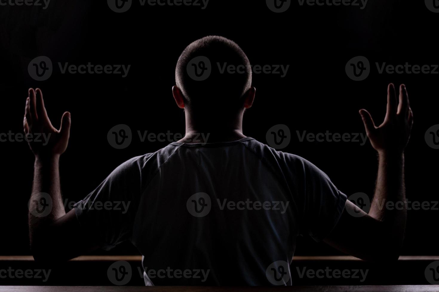 Silhouette eines jungen Mannes, der in der Kirche sitzt und mit erhobenen Händen betet foto