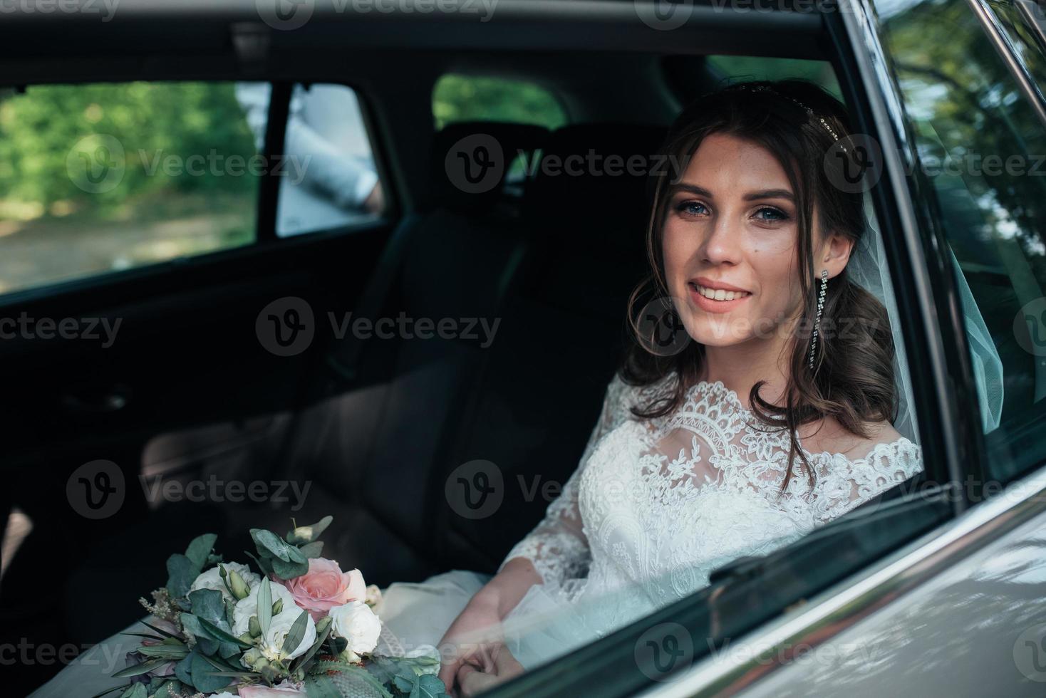 Hochzeitsfoto der Braut, die im Auto mit einem Blumenstrauß sitzt foto