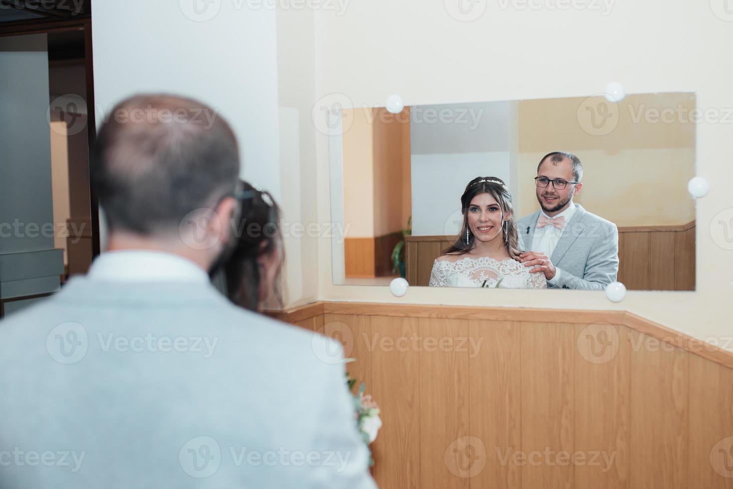 Braut und Bräutigam umarmen sich und schauen in ihrem Spiegelbild in den Spiegel foto