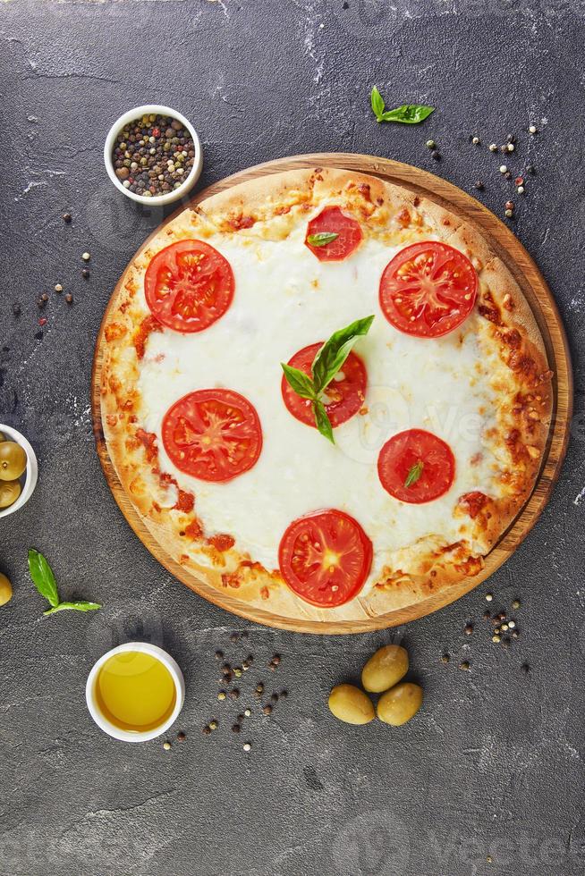 italienische Pizza und Zutaten zum Kochen auf einem schwarzen Betonhintergrund Tomatenoliven Basilikum und Gewürze foto