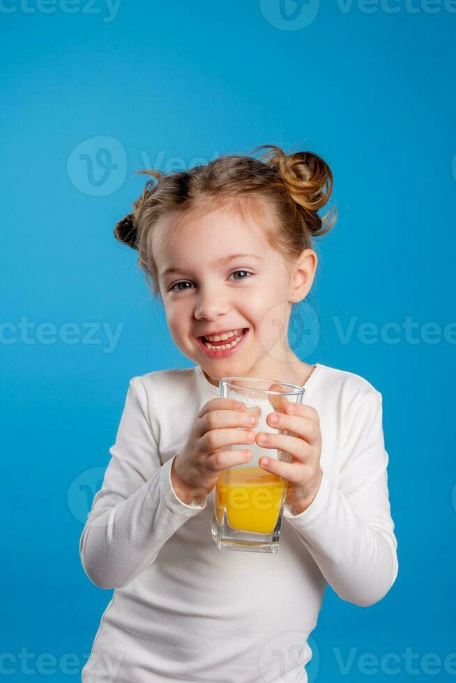 Porträt von ein wenig Mädchen von slawisch Aussehen Trinken Orange Saft auf ein Blau Hintergrund foto