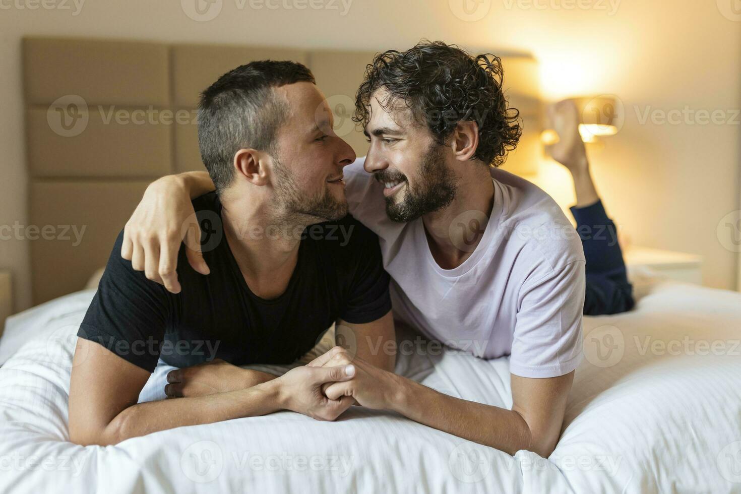 glücklich Fröhlich Paar Lügen Nieder auf das Bett beim heim, umarmen und flirten. lgbt Fröhlich Paar Liebe Momente Glück Konzept foto