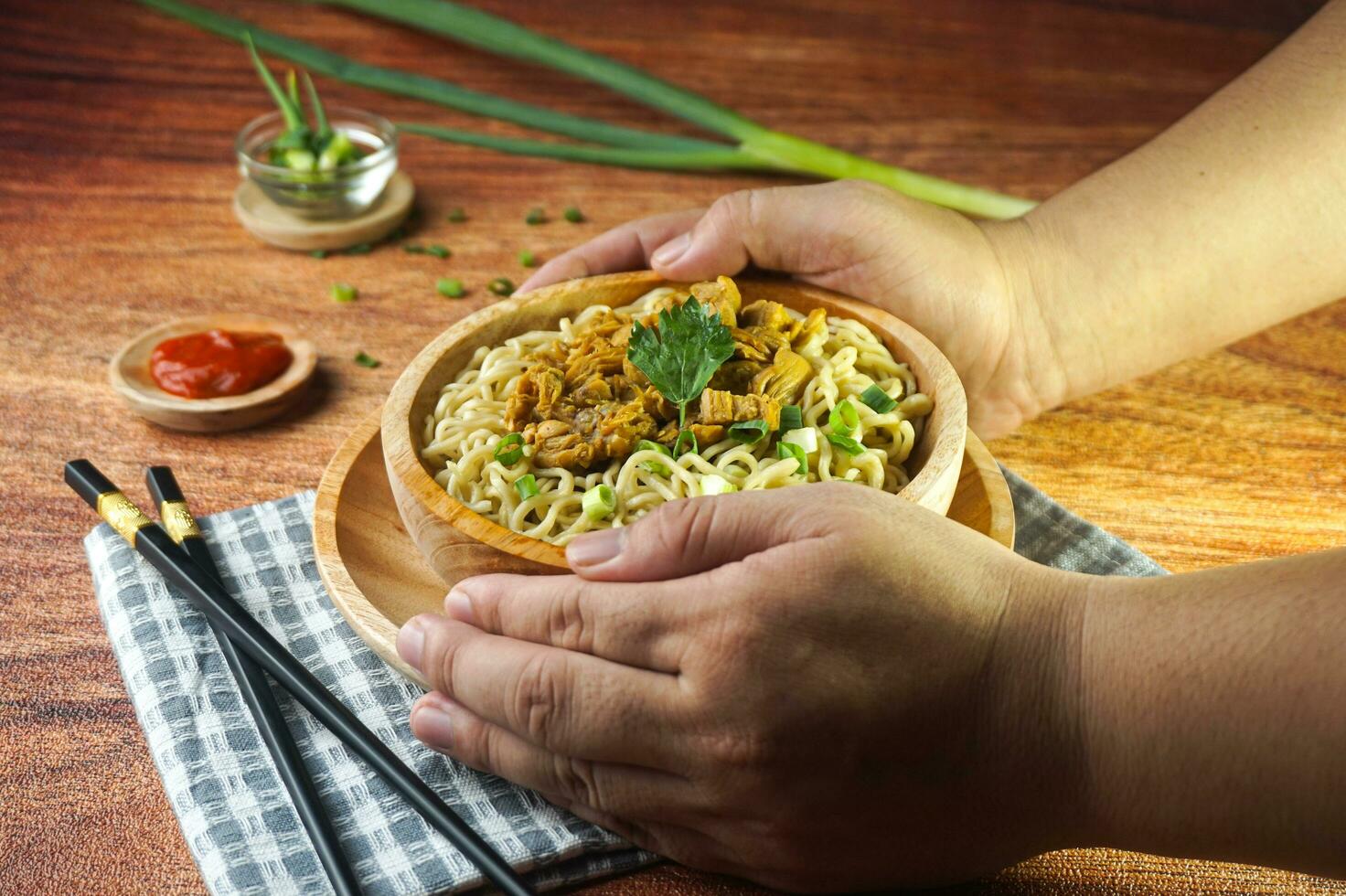 Nudeln mit Huhn, im Indonesien es ist bekannt wie mie ayam. serviert mit Grün Gemüse Chili Soße im ein Schüssel auf hölzern Hintergrund durch Hand foto