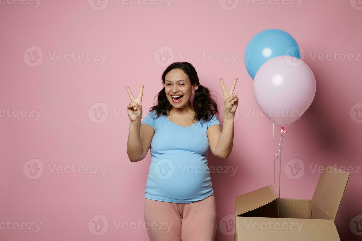 schwanger Frau lächelt und zeigt an zwei Finger beim Kamera, Gefühl positiv Emotionen erwarten Zwillinge. Geschlecht verraten Party. foto