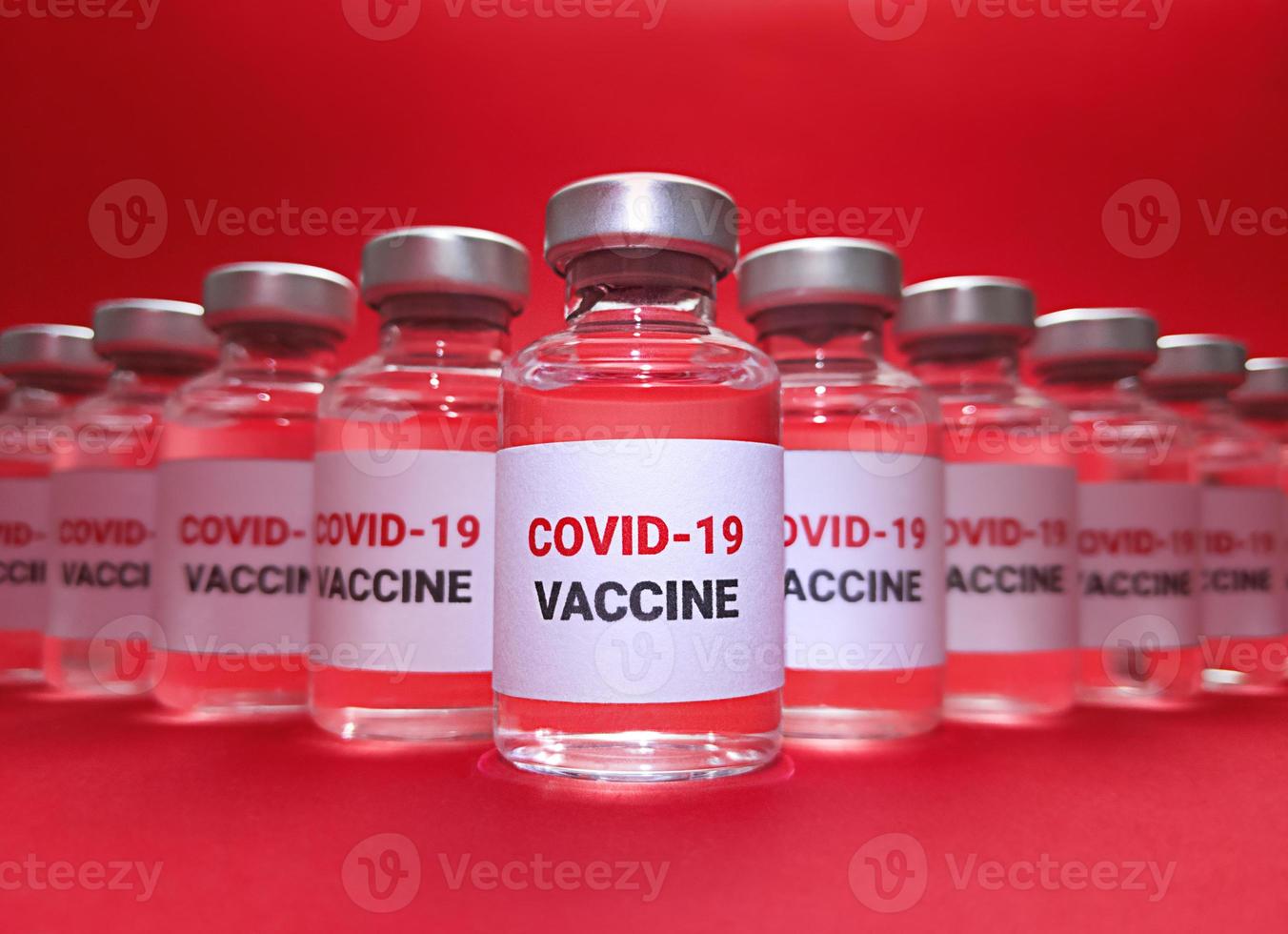 viele Fläschchen mit Covid 19-Impfstoff auf rotem Grund foto