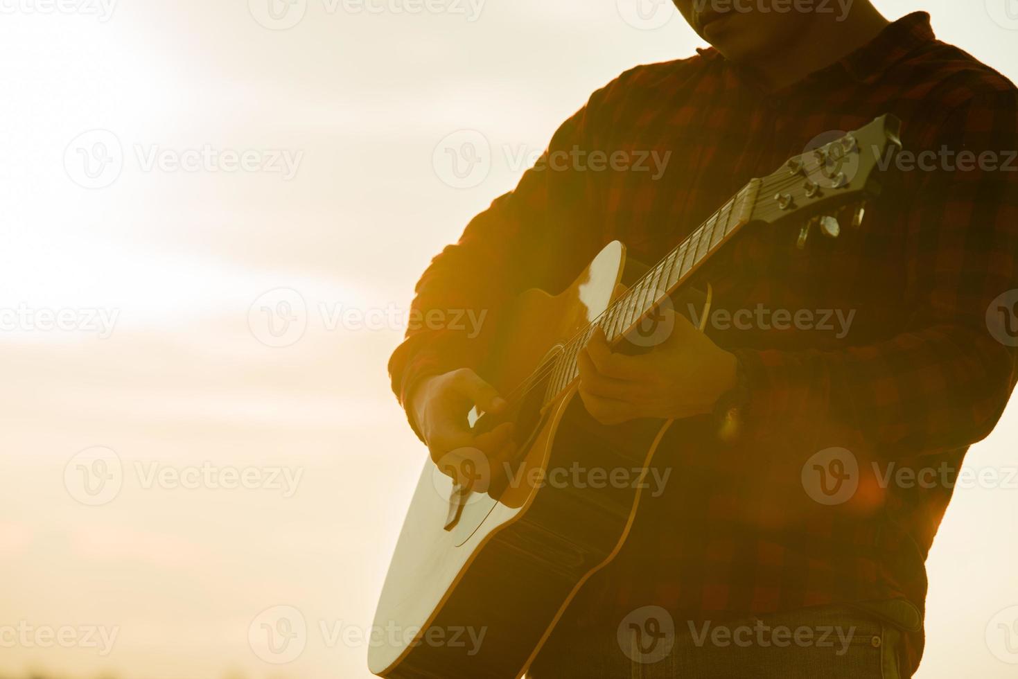 asiatische Mannakustikgitarre mit Schattenbild mit Sonnenunterganghintergrund foto