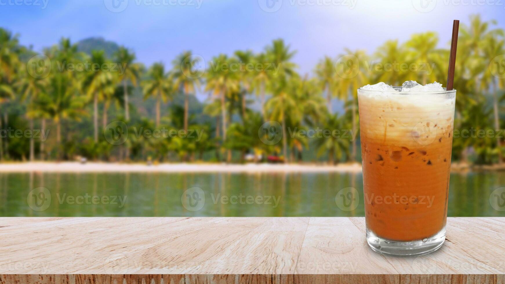 vereist thailändisch Milch Tee im Glas, Milch Eis Tee, Cheddar ist ein traditionell thailändisch trinken auf hölzern Tabelle mit Strand Landschaft Natur Hintergrund, Sommer- Getränke mit vereist foto