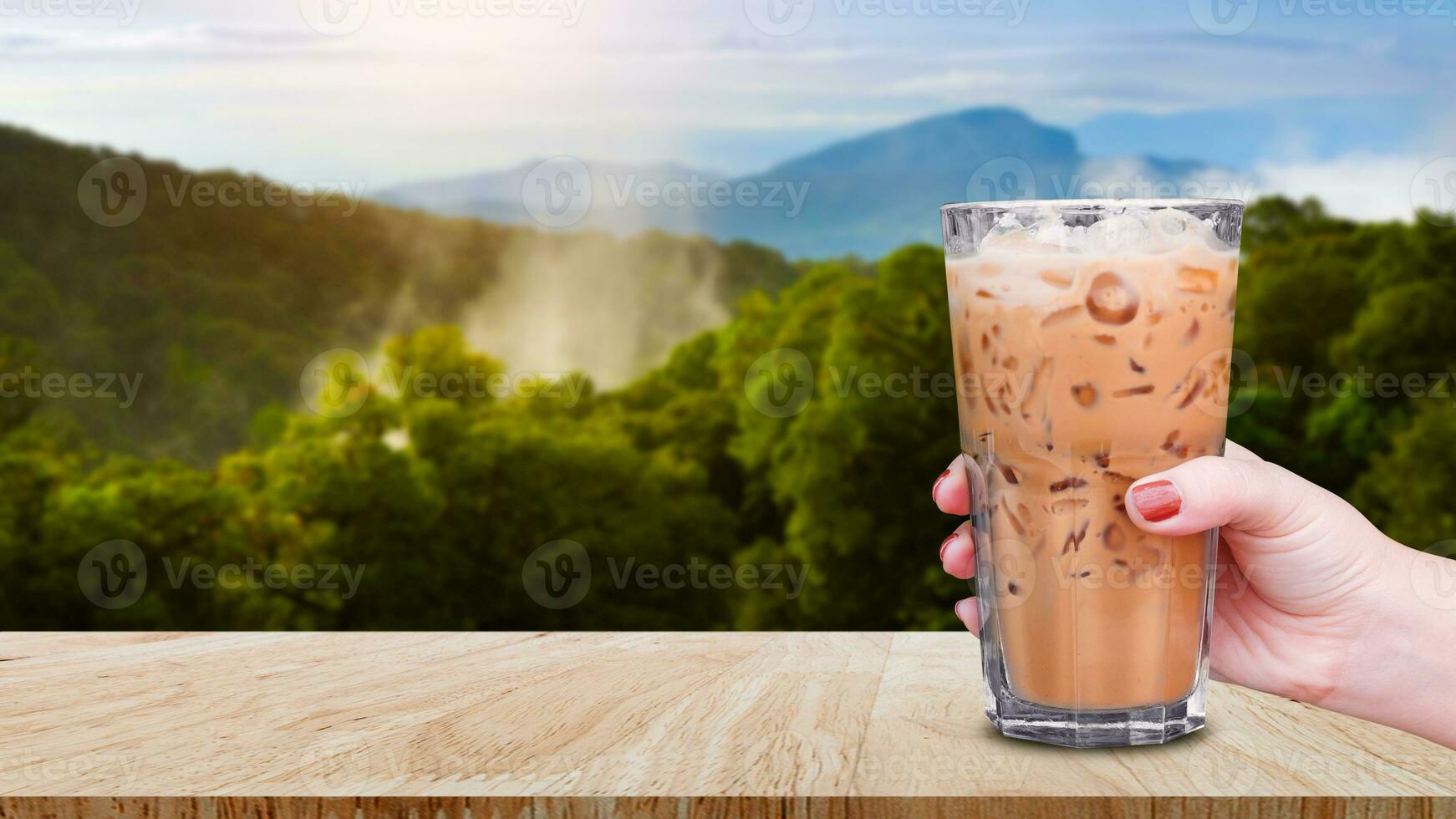 Hand halten das Glas vereist Kaffee auf hölzern Tabelle mit Landschaft Natur Hintergrund, Eis Latté Kaffee foto