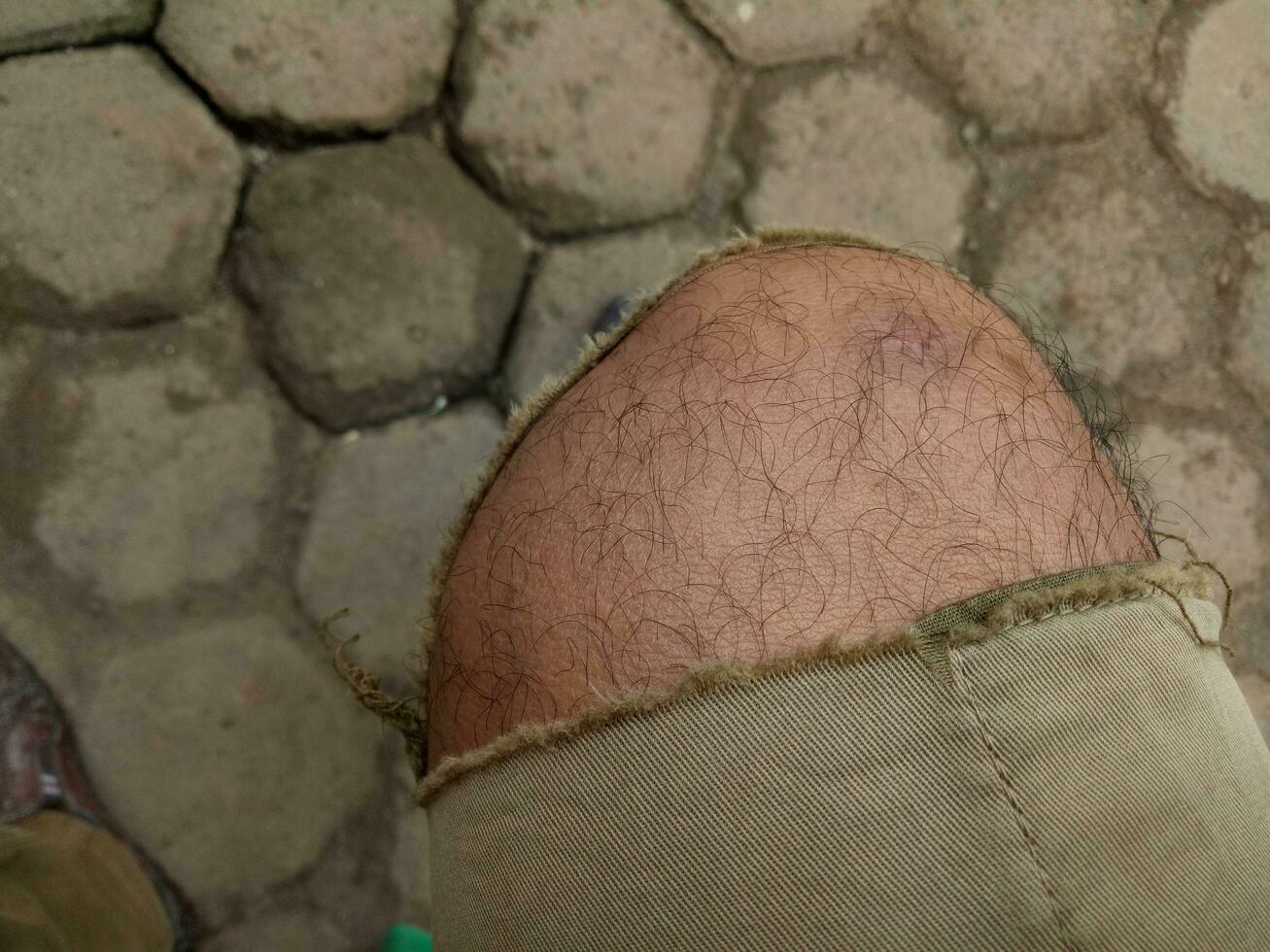 Foto von ein Jungs Bein tragen zerrissen braun Hose gegen ein sechseckig Backstein Fußboden im das Hintergrund