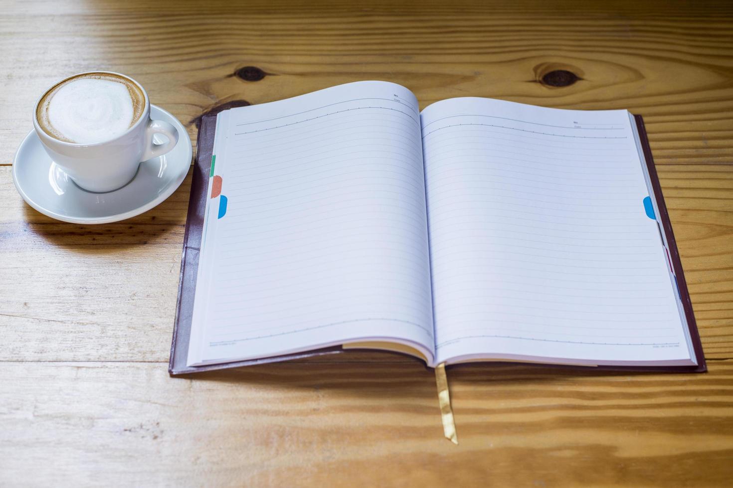 Notizbuch mit Tasse Kaffee auf Holzschreibtisch foto