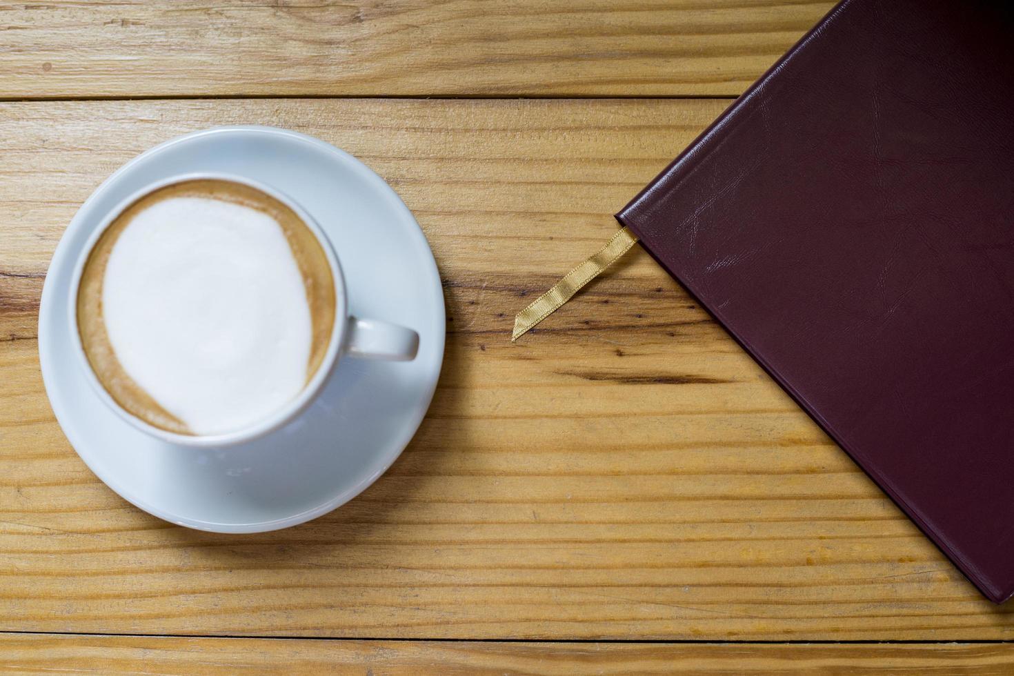 Notizbuch mit Tasse Kaffee auf Holzschreibtisch foto