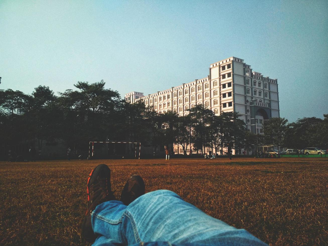 Person in blauen Jeans, die auf braunem Grasfeld liegt, das weißes mehrstöckiges Gebäude betrachtet foto