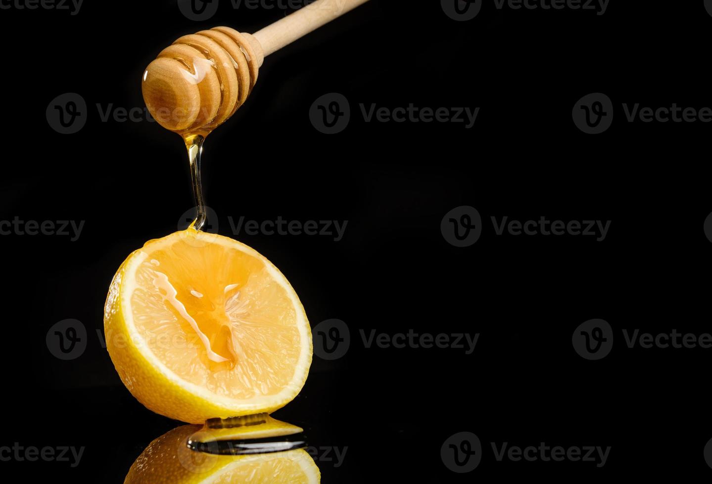 Honig fließt von einem Löffel zu einer Zitrone, die auf einem schwarzen Hintergrund mit Kopierraum liegt foto