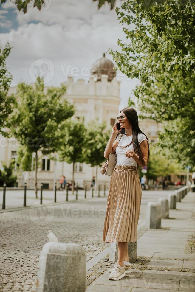 junge Frau, die ein Mobiltelefon beim Gehen auf der Straße benutzt foto