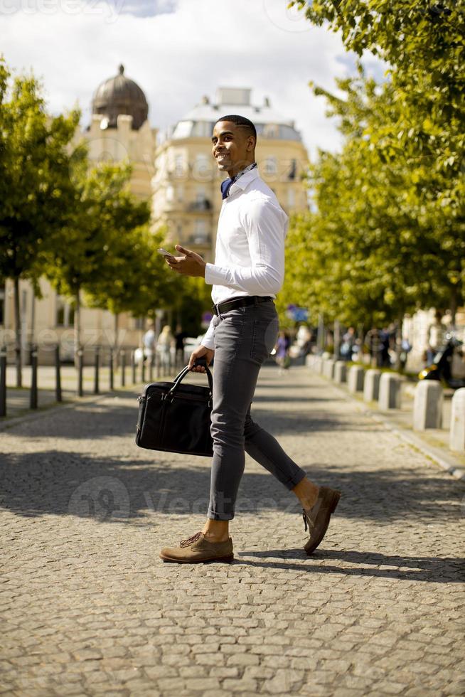 junger afroamerikanischer Geschäftsmann, der ein Mobiltelefon beim Überqueren einer Straße verwendet foto
