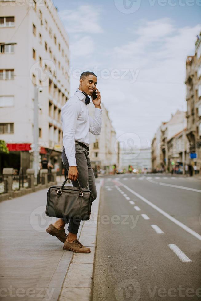 junger afroamerikanischer Geschäftsmann, der ein Mobiltelefon beim Überqueren einer Straße verwendet foto