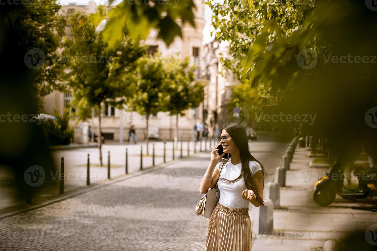 junge Frau, die ein Mobiltelefon beim Gehen auf der Straße benutzt foto