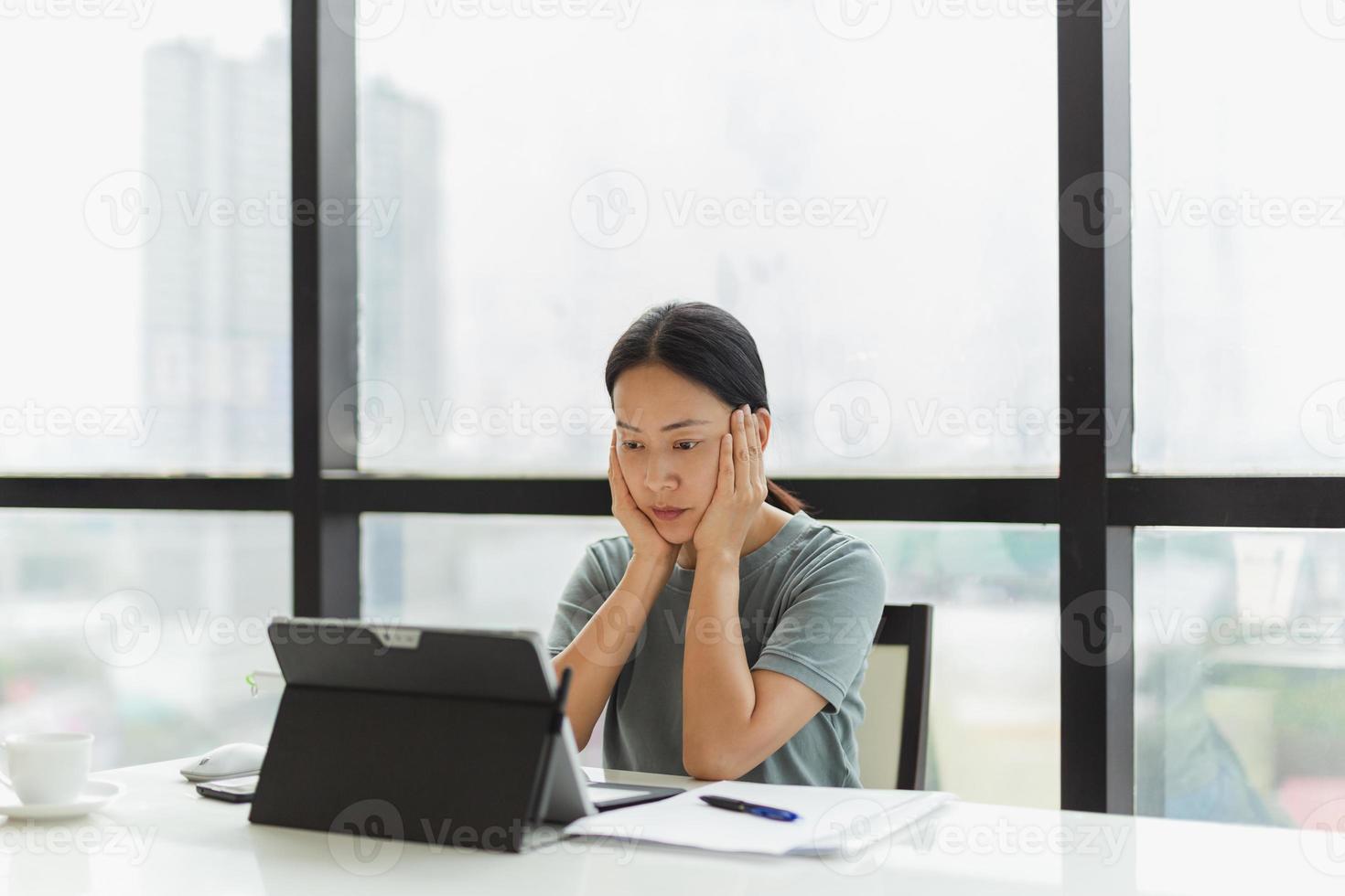 Porträt der Geschäftsfrau, die auf Laptop mit Händen auf ihrer Wange arbeitet foto