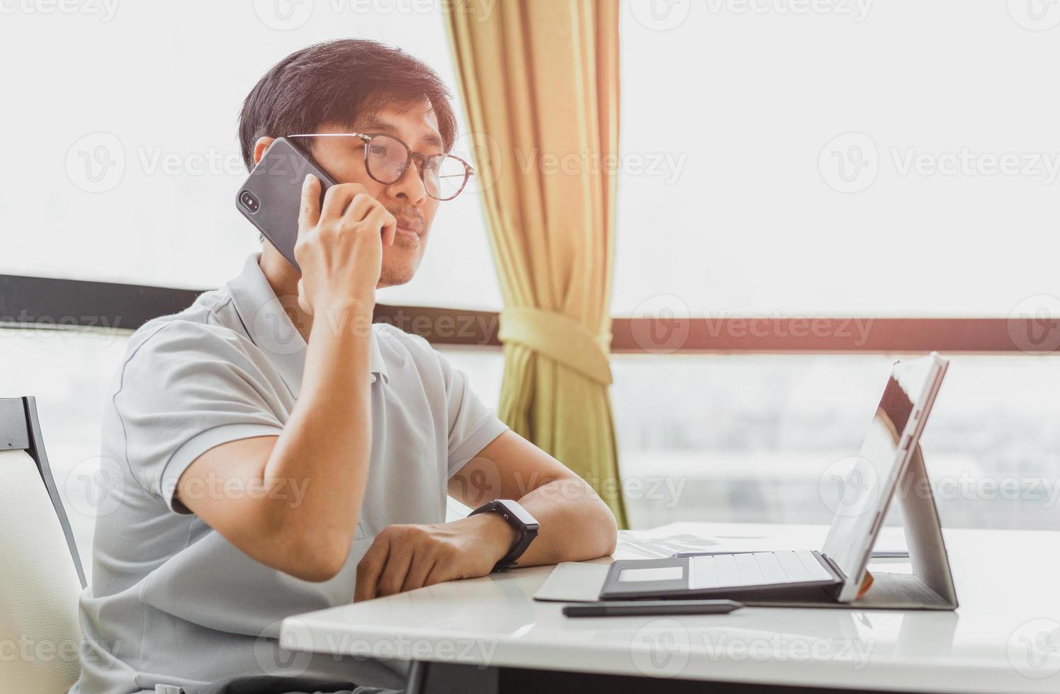 Mann, der auf Mobiltelefon spricht, während Laptop-Computer arbeitet foto