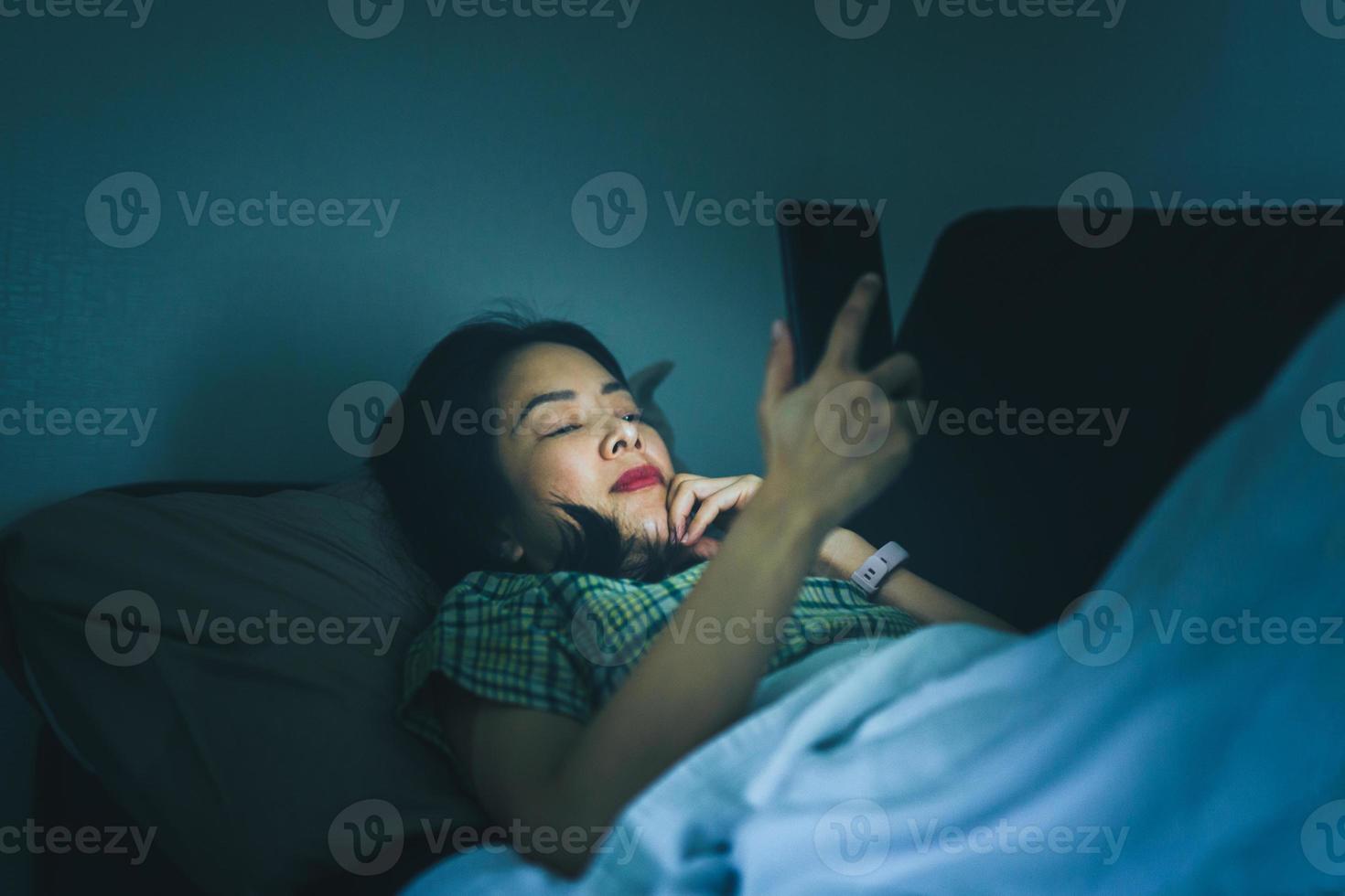 Frau, die nachts auf der Couch mit dem Mobiltelefon liegt foto